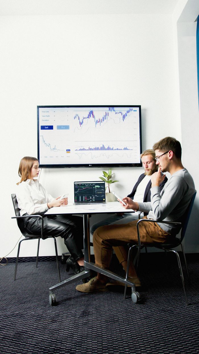 services-04 Three business professionals in a meeting room discussing financial charts displayed on a screen.