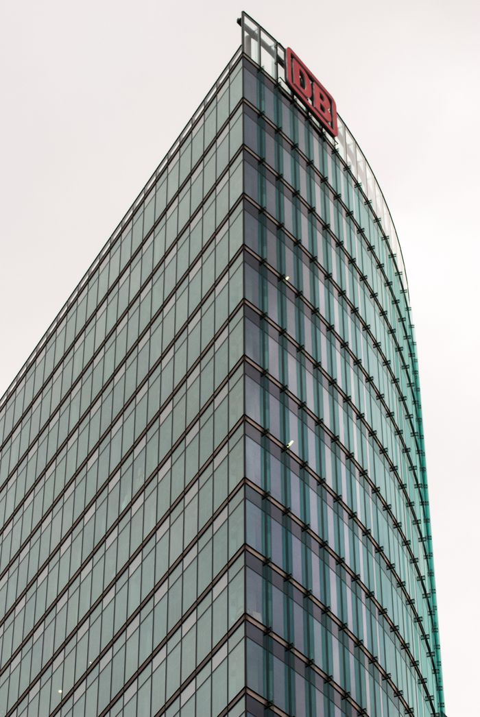 about-us Low angle view of a modern skyscraper with glass panels and a prominent logo against an overcast sky.