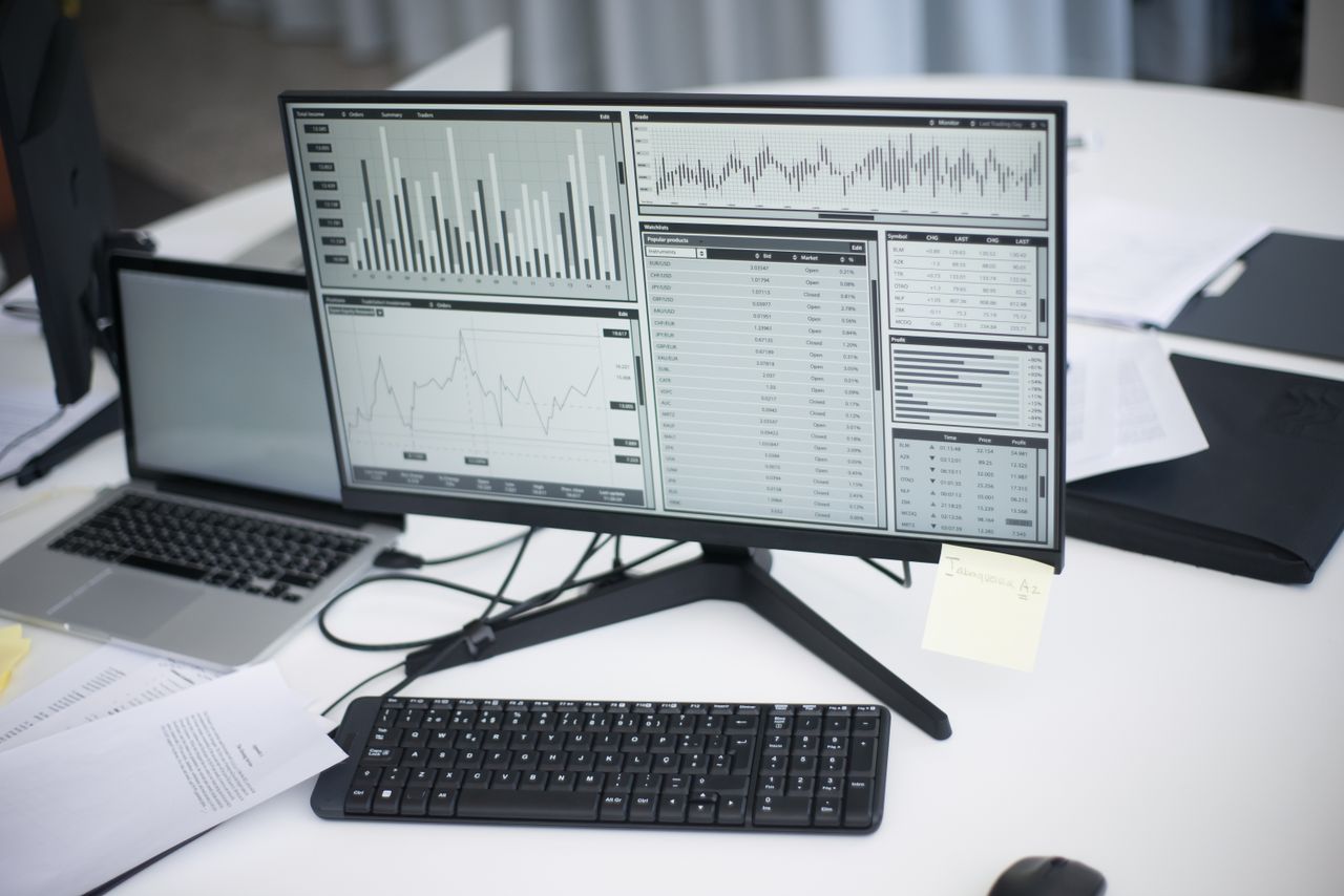 our-story A professional workspace featuring computers and analytical graphs on a monitor, symbolizing modern business environment.